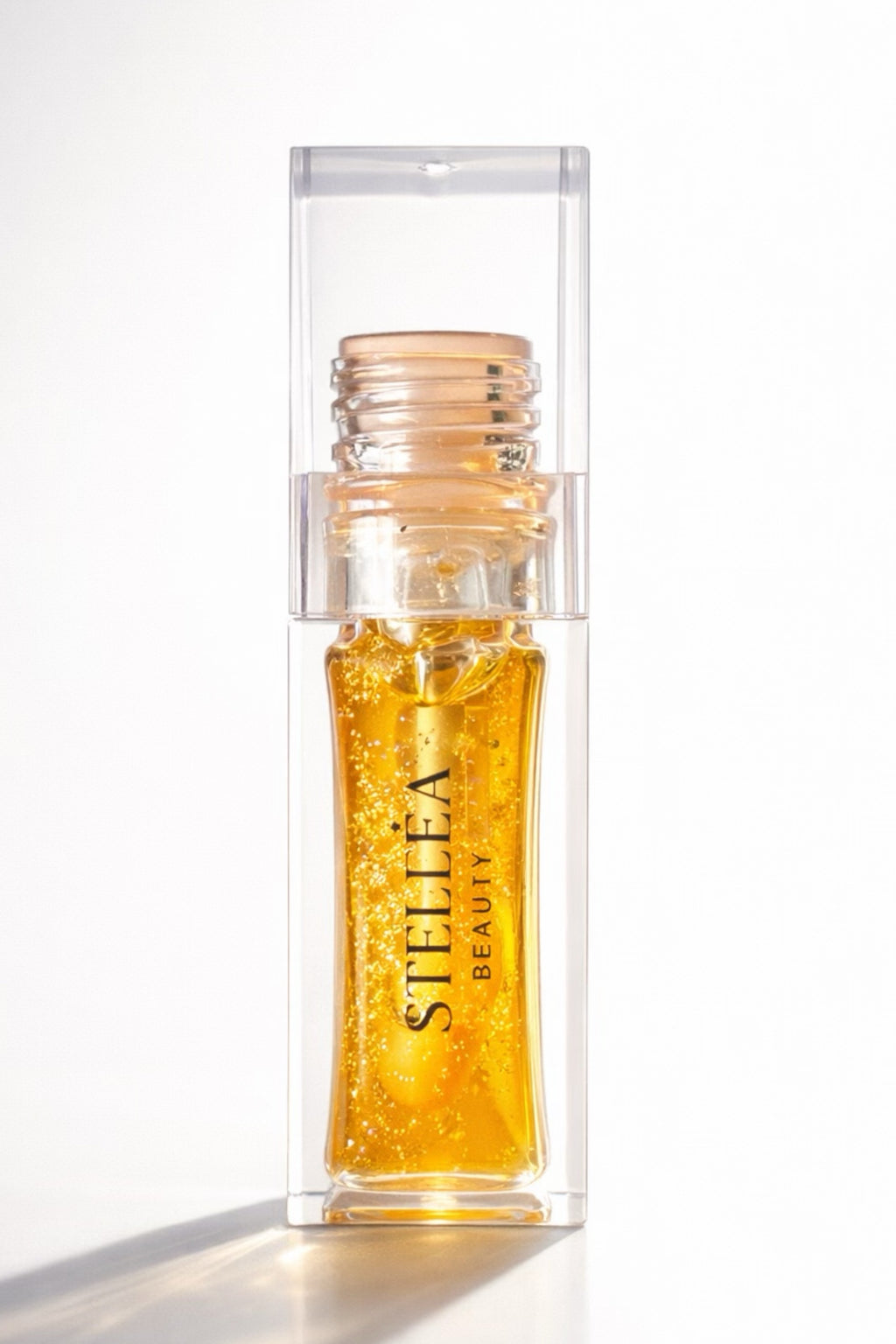 Huile à lèvres brillante STELLEA Coral en flacon transparent avec texture dorée aux reflets glossy